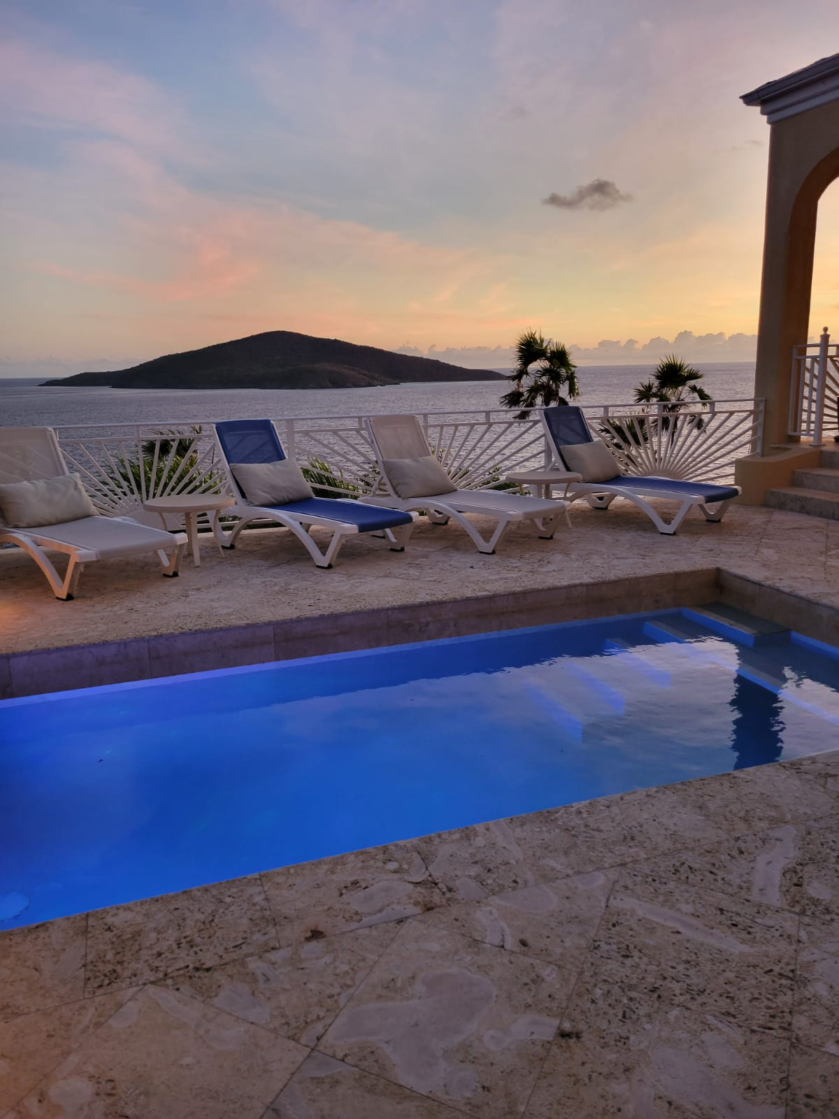 sun setting over ocean behind deck chairs around villa private pool